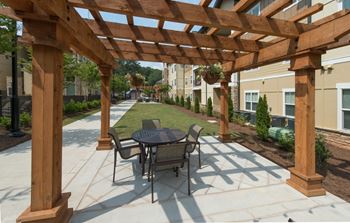 A wooden pergola with a table and chairs is in the foreground of a patio area.